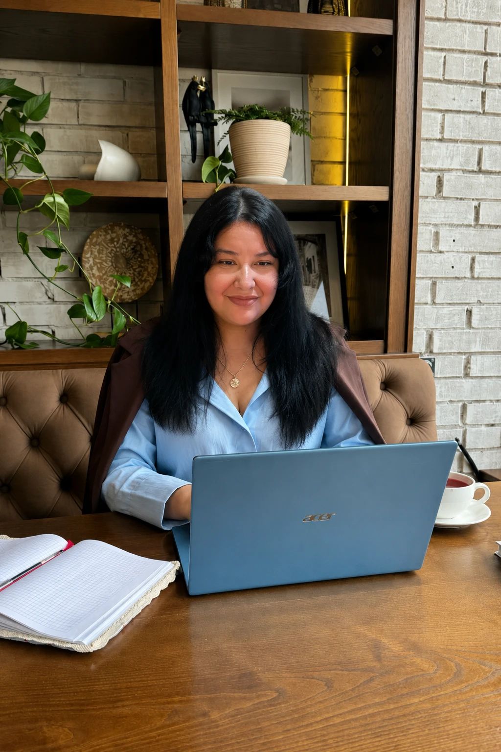 Lorena Tigani trabajando en su laptop, con un cuaderno abierto y una taza de té